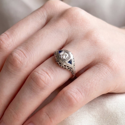 Art Deco sapphire and diamond ring in 18k white gold with intricate vintage design, featuring sparkling gemstones.